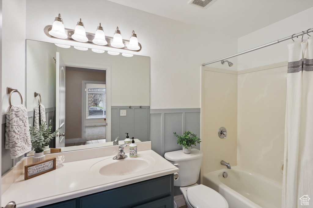 Full bath with shower / bath combo, a wainscoted wall, a decorative wall, toilet, and vanity
