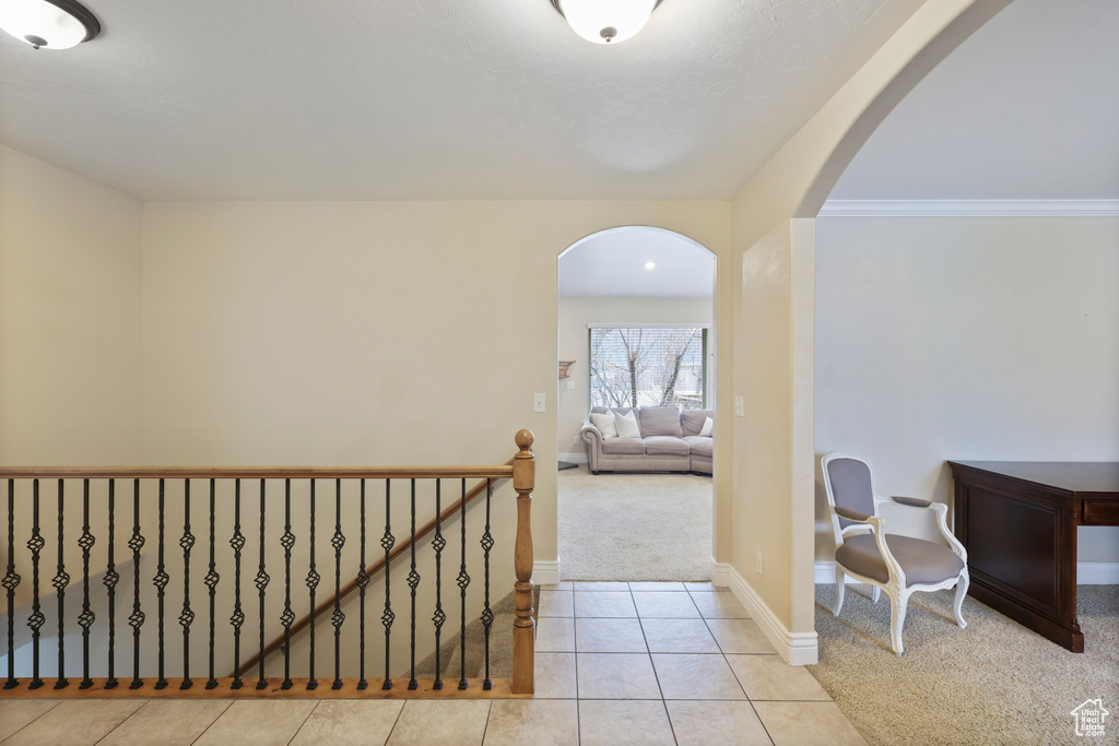 Hallway featuring baseboards, arched walkways, tile patterned flooring, and carpet
