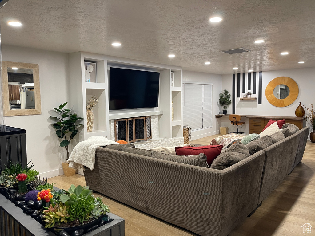 Living area with a textured ceiling, light wood-style flooring, and recessed lighting