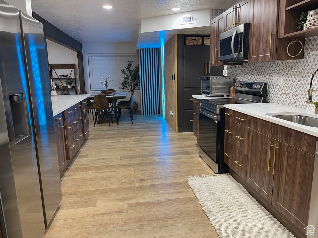 Kitchen featuring light countertops, a sink, tasteful backsplash, light wood-type flooring, and stainless steel appliances