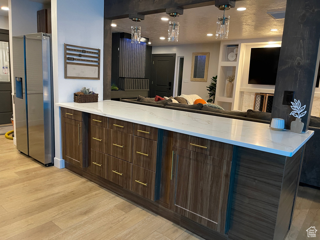 Kitchen with open floor plan, light wood-style floors, stainless steel fridge, and a peninsula