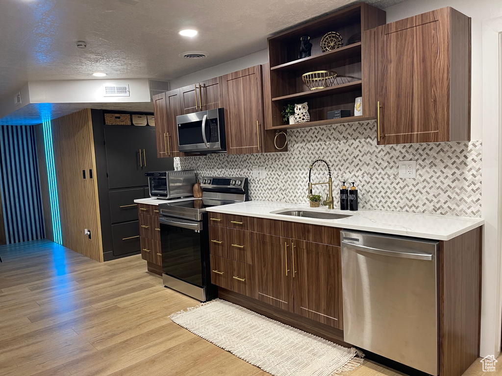 Kitchen featuring light countertops, open shelves, light wood-type flooring, a sink, and appliances with stainless steel finishes