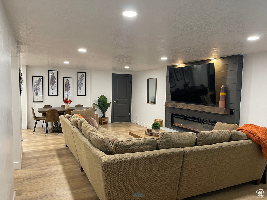 Living room with recessed lighting, baseboards, a textured ceiling, light wood finished floors, and a glass covered fireplace
