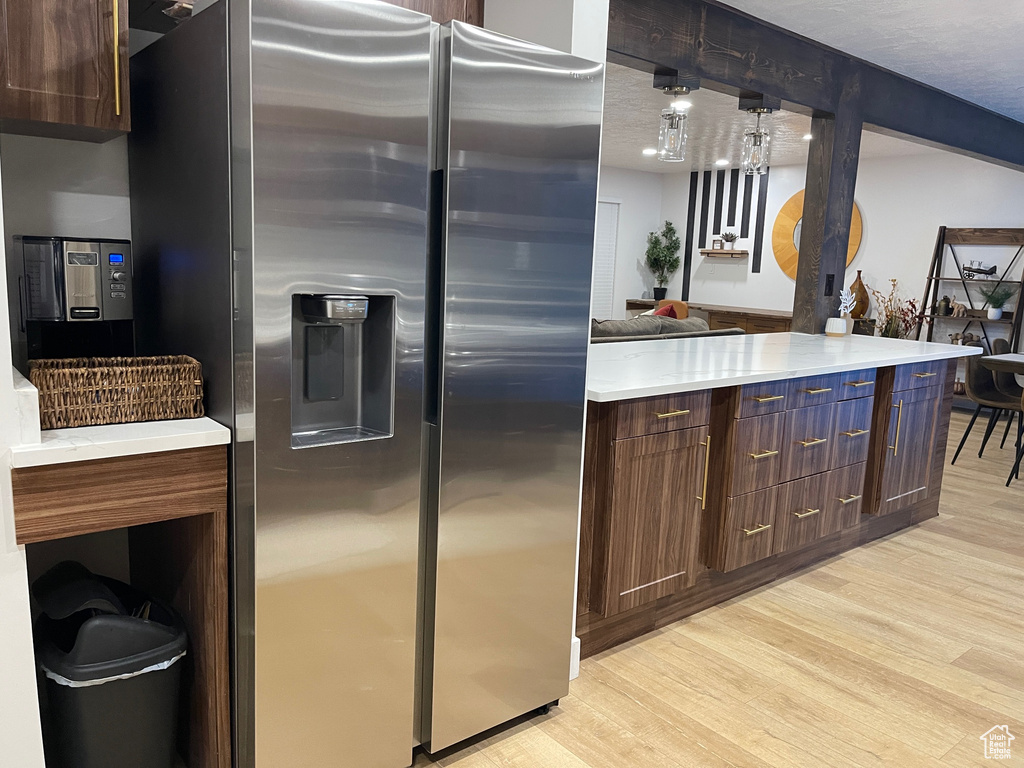 Kitchen featuring light countertops, light wood-style flooring, stainless steel refrigerator with ice dispenser, and dark brown cabinets