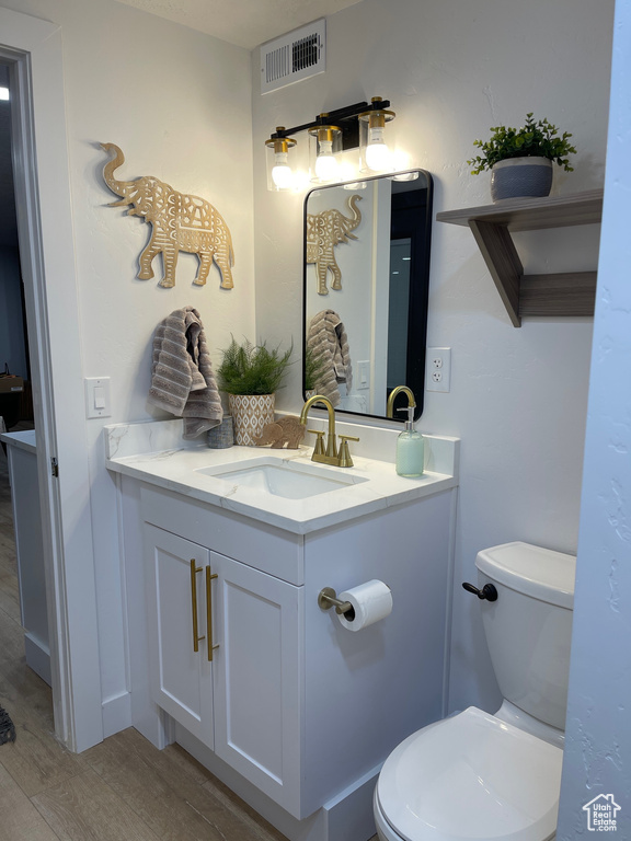 Half bathroom with visible vents, wood finished floors, toilet, and vanity