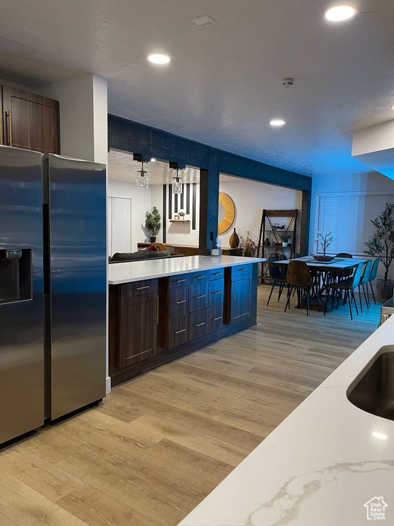 Kitchen with recessed lighting, light wood-type flooring, stainless steel fridge with ice dispenser, a sink, and dark brown cabinetry