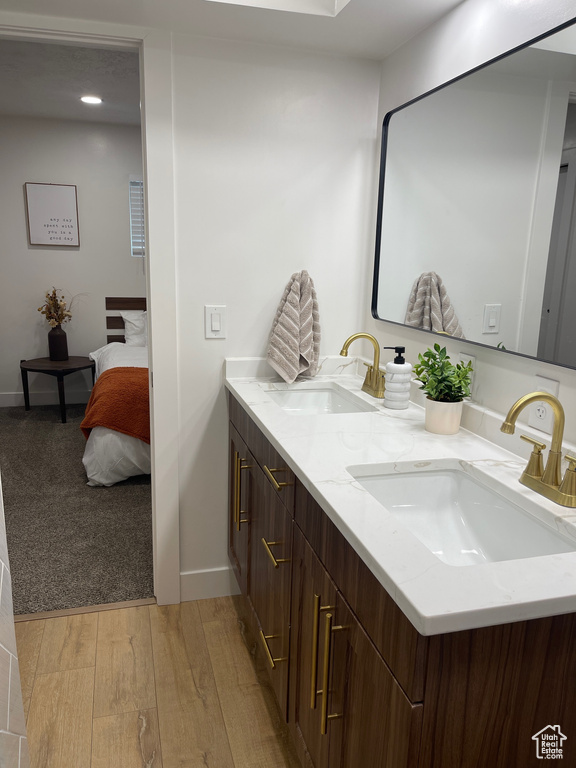 Ensuite bathroom with baseboards, double vanity, a sink, and wood finished floors