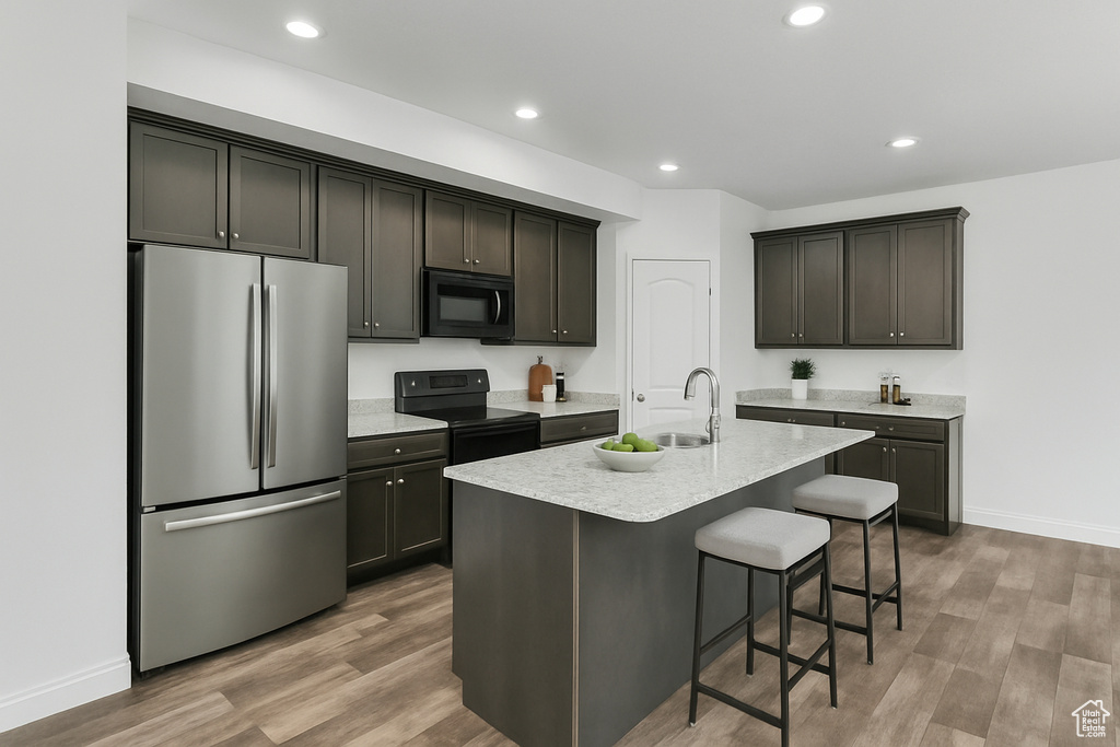 Kitchen featuring a kitchen island with sink, wood finished floors, a breakfast bar area, a sink, and black appliances