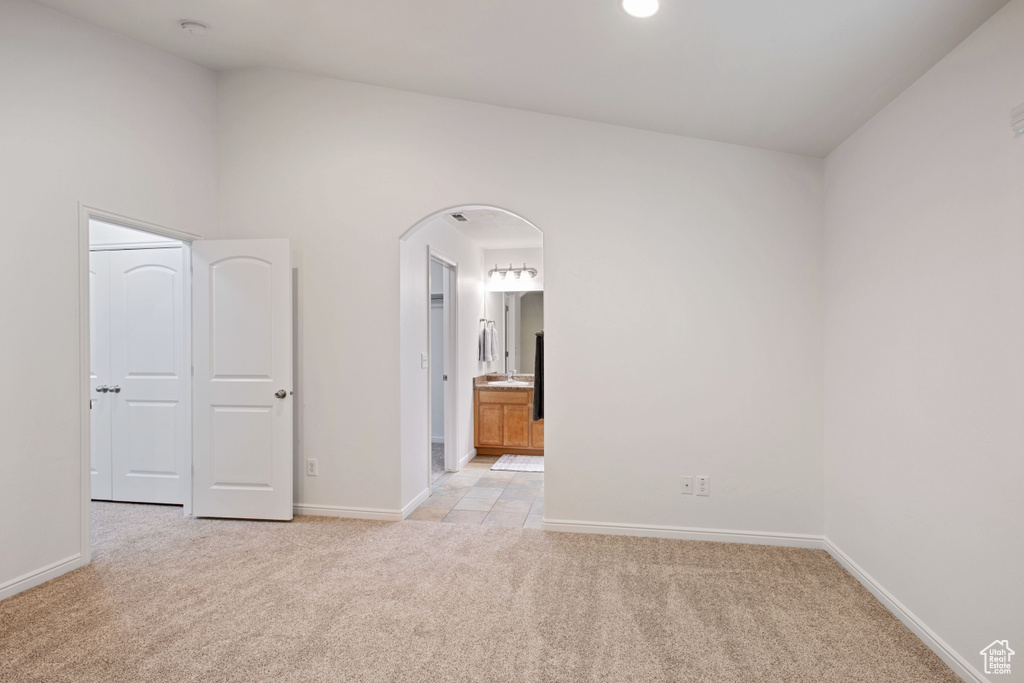 Unfurnished room featuring arched walkways, baseboards, and light colored carpet