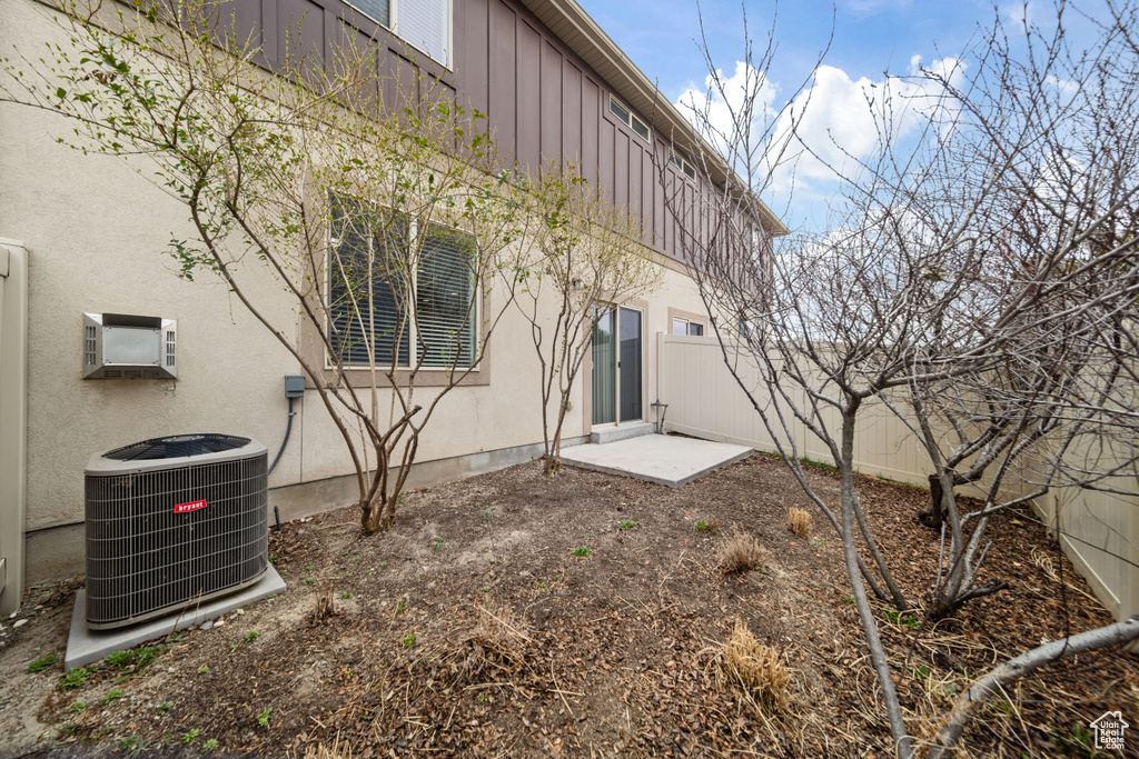 Rear view of property featuring a wall mounted AC, stucco siding, fence, board and batten siding, and central AC