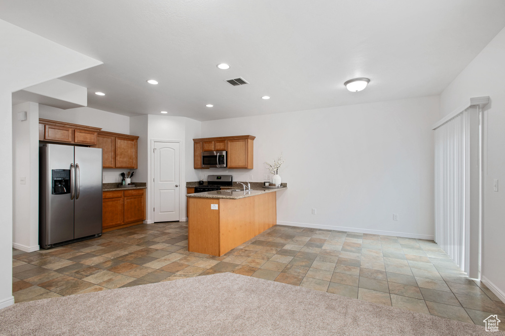 Kitchen with a peninsula, brown cabinetry, stainless steel appliances, visible vents, and recessed lighting