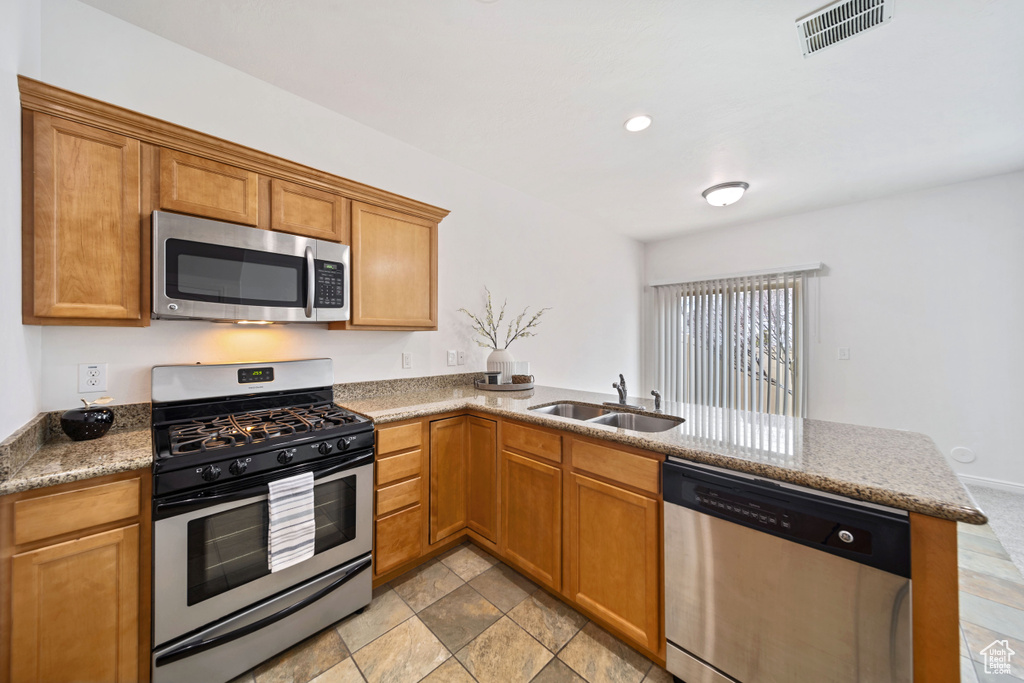 Kitchen featuring a sink, a peninsula, brown cabinets, stainless steel appliances, and visible vents