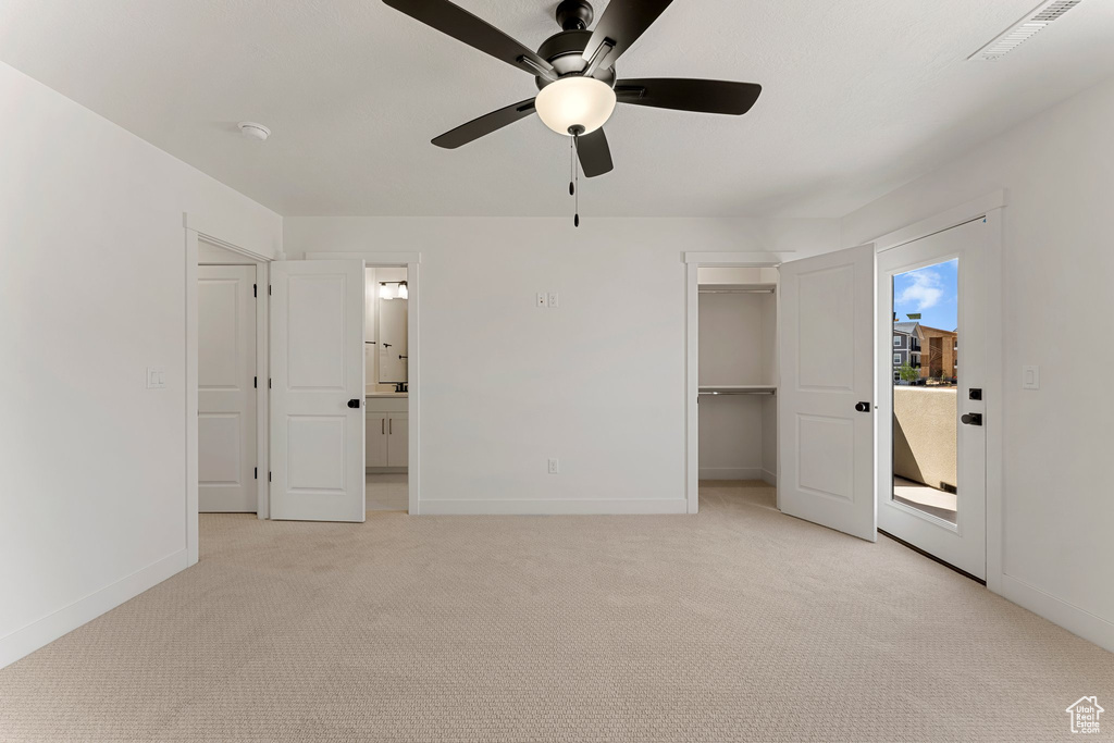 Unfurnished bedroom with light colored carpet, a walk in closet, a ceiling fan, and ensuite bath