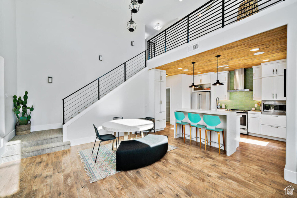 Dining room featuring stairs, light wood-type flooring, baseboards, a towering ceiling, and visible vents