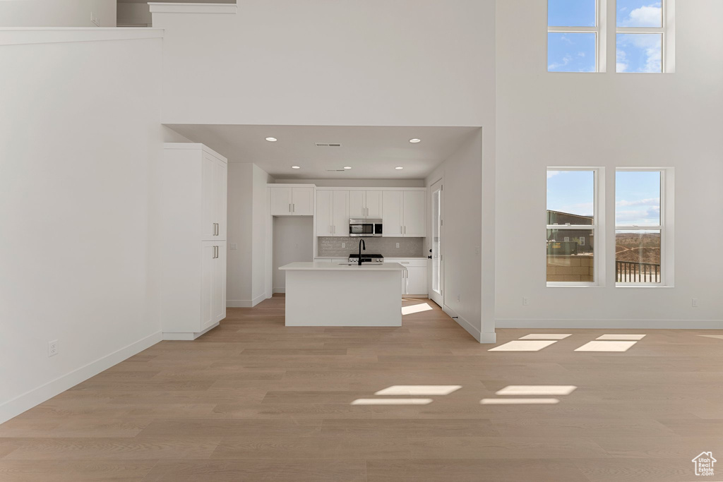 Unfurnished living room with a high ceiling, light wood finished floors, and recessed lighting