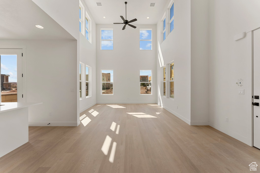 Unfurnished living room with a ceiling fan, light wood-style flooring, recessed lighting, and a high ceiling