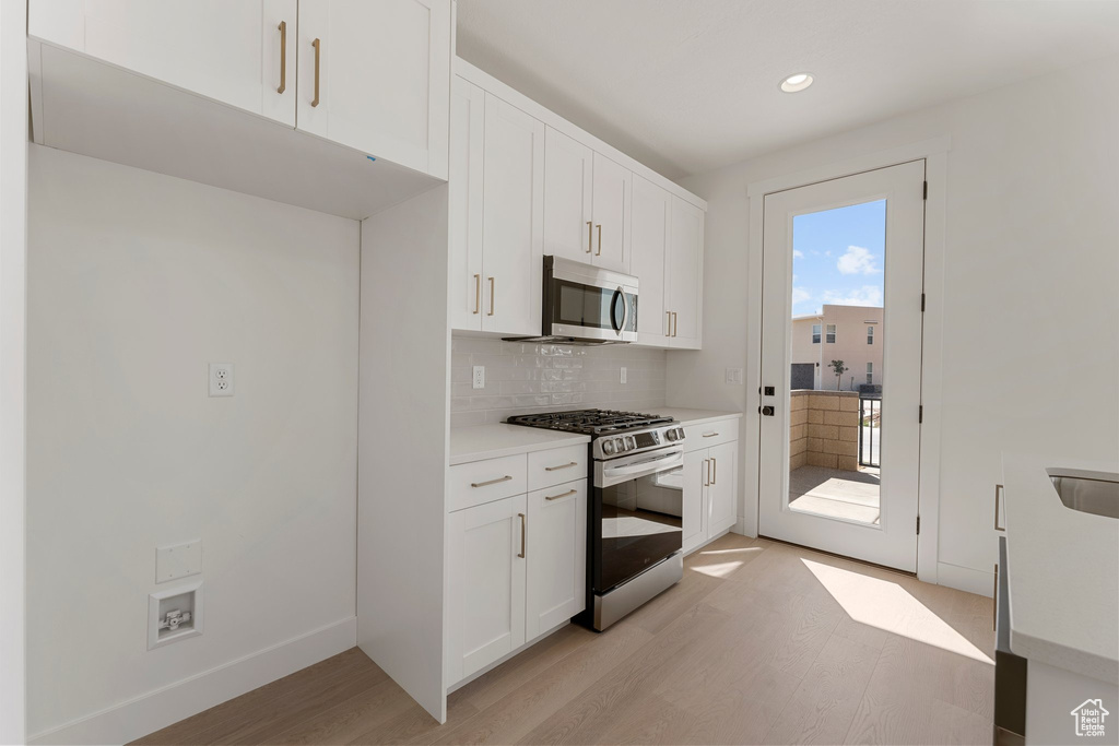 Kitchen featuring appliances with stainless steel finishes, light wood finished floors, tasteful backsplash, light countertops, and white cabinets