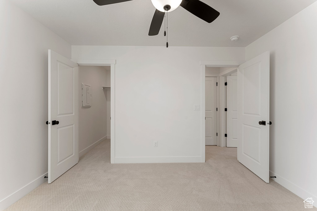Unfurnished bedroom with light carpet, a walk in closet, ceiling fan, and a closet