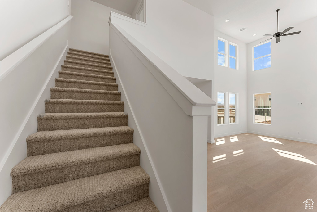 Stairs with wood finished floors, ceiling fan, recessed lighting, and a high ceiling