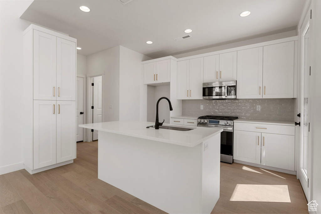 Kitchen with appliances with stainless steel finishes, light wood-style floors, backsplash, recessed lighting, and white cabinetry