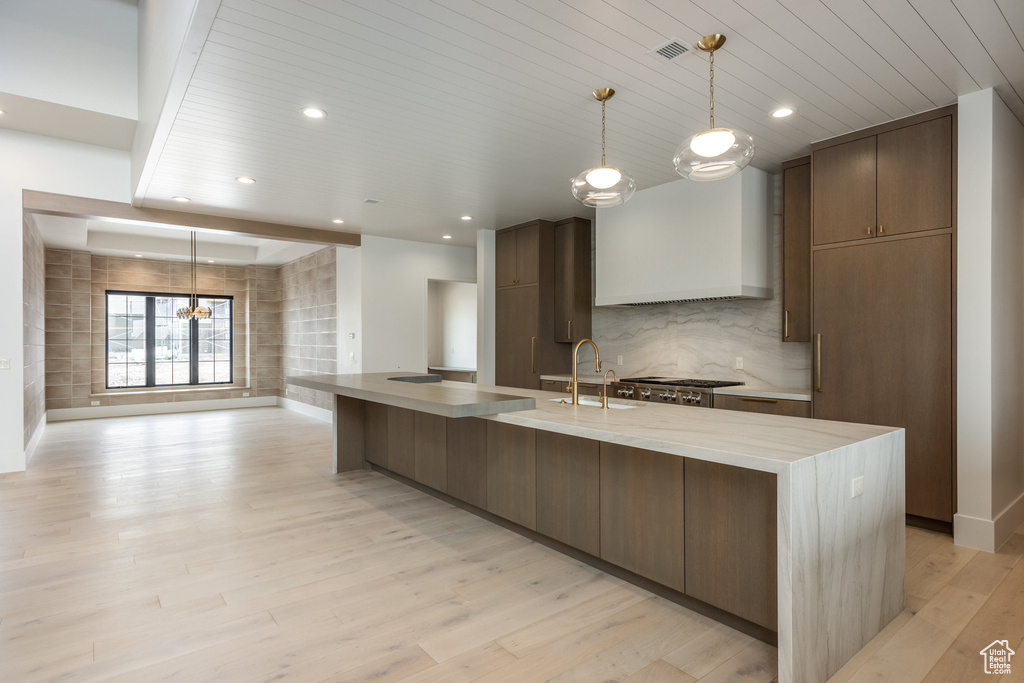Kitchen with decorative backsplash, stainless steel gas stovetop, custom exhaust hood, light wood finished floors, and wooden ceiling