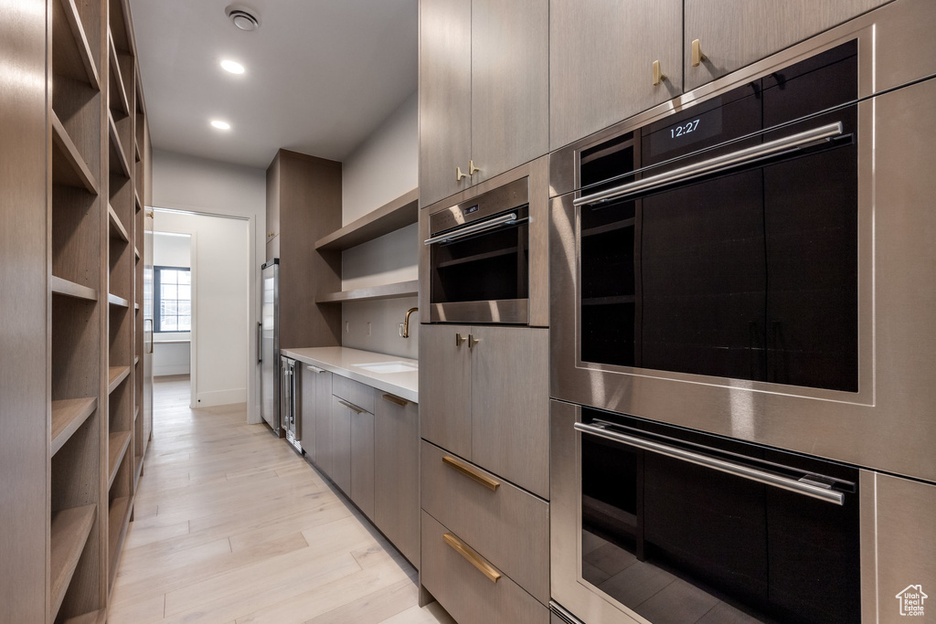 Kitchen with light countertops, modern cabinets, a sink, open shelves, and light wood-type flooring