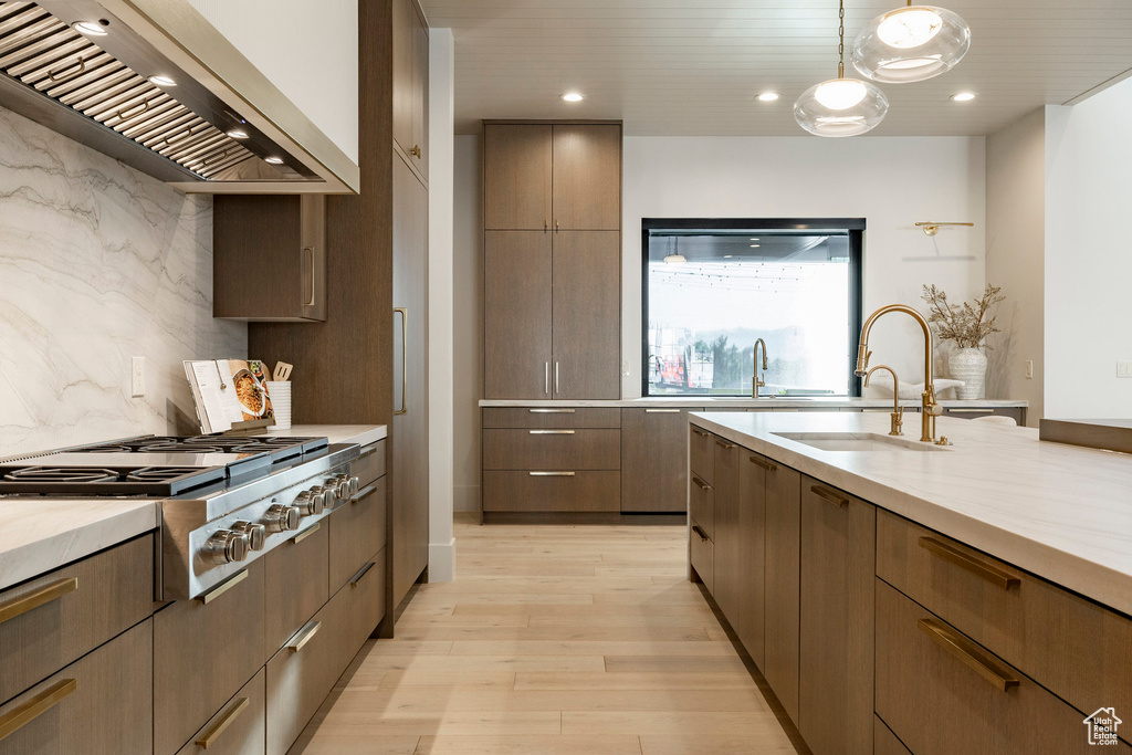 Kitchen with wall chimney range hood, stainless steel gas cooktop, a sink, light wood-style flooring, and modern cabinets