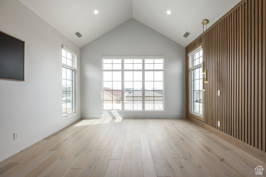 Empty room with high vaulted ceiling, light wood-style flooring, and visible vents