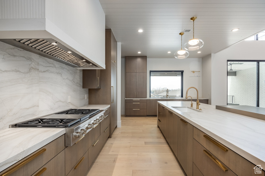 Kitchen with modern cabinets, stainless steel gas cooktop, a sink, light wood-style floors, and custom range hood