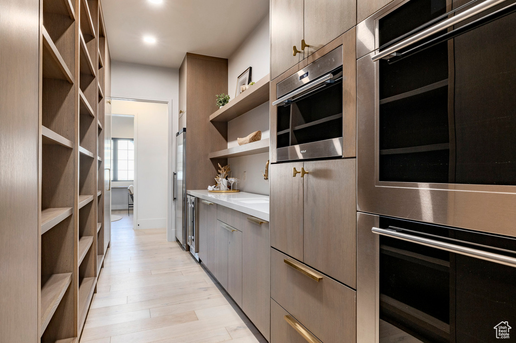 Kitchen with open shelves, double oven, light countertops, modern cabinets, and light wood finished floors