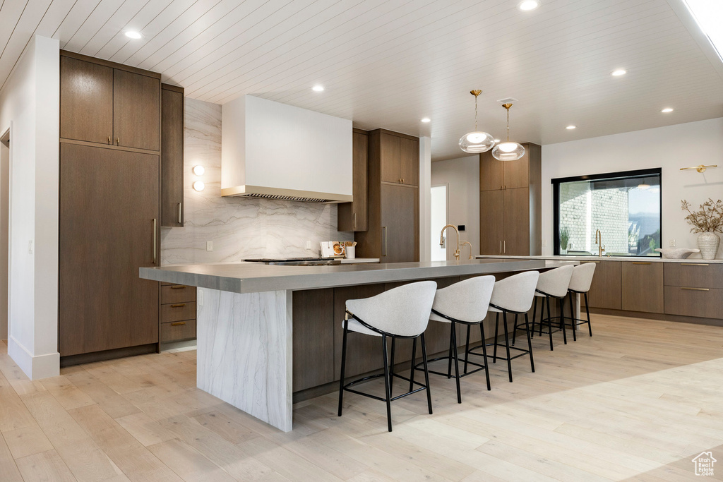 Kitchen featuring modern cabinets, wall chimney exhaust hood, a breakfast bar, light wood-style floors, and recessed lighting