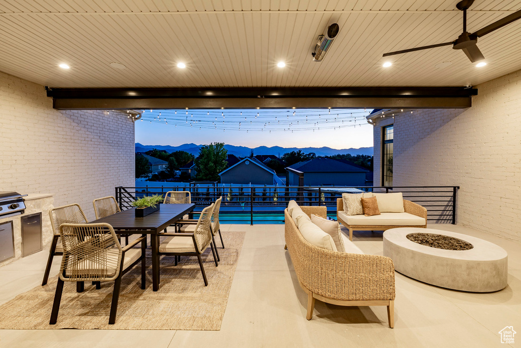 Patio terrace at dusk with a mountain view, outdoor dining space, a ceiling fan, and an outdoor living space with a fire pit