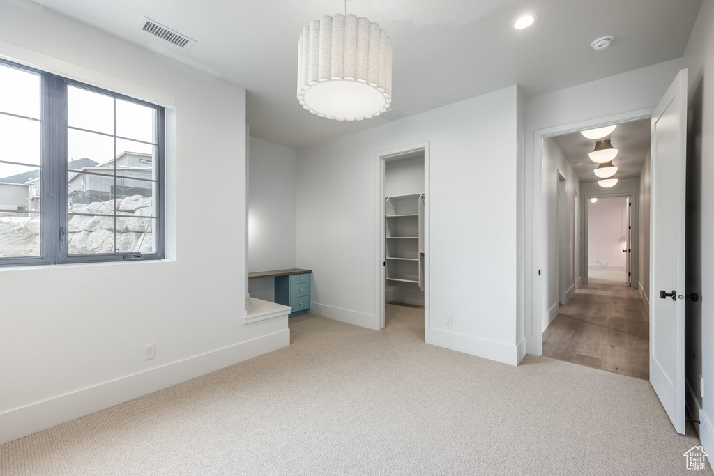 Unfurnished bedroom with a closet, visible vents, baseboards, light carpet, and a walk in closet