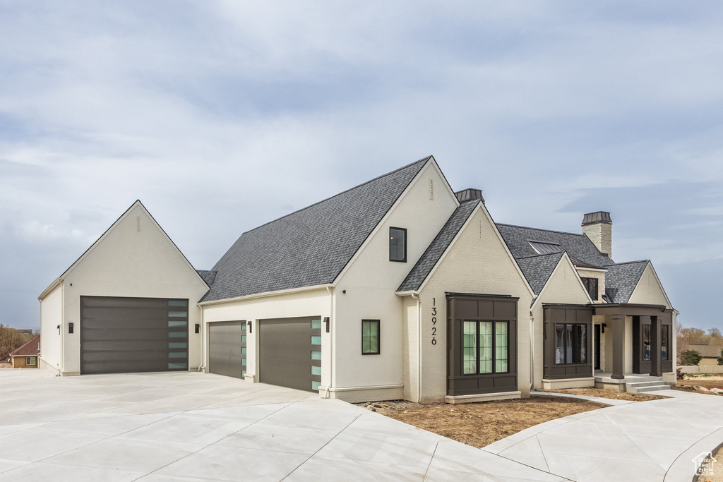 View of front of home featuring roof with shingles, concrete driveway, a chimney, stucco siding, and an attached garage