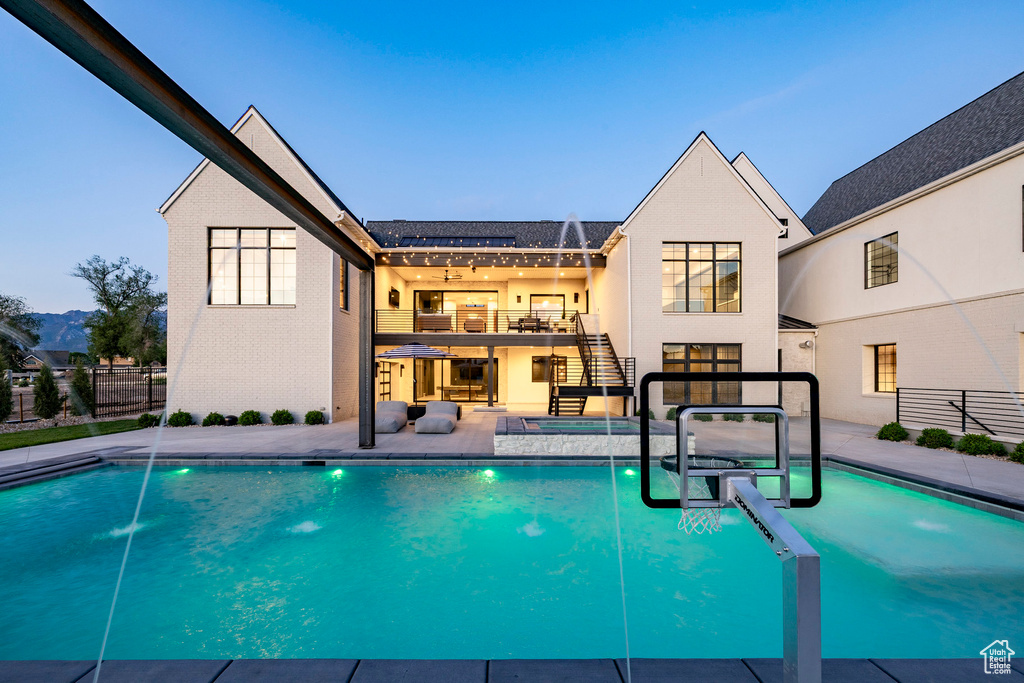 Rear view of property featuring stairway, a patio, a pool with connected hot tub, stucco siding, and a balcony