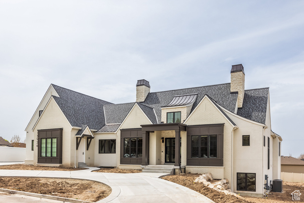 Modern inspired farmhouse with a standing seam roof, a chimney, cooling unit, brick siding, and metal roof