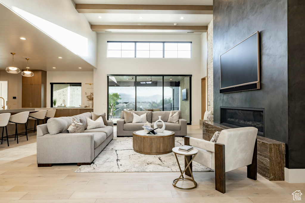 Living room featuring beam ceiling, a towering ceiling, light wood-type flooring, a fireplace, and recessed lighting