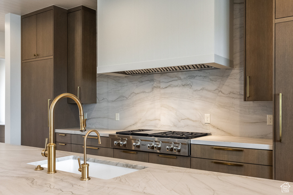 Kitchen with stainless steel gas cooktop, a sink, light stone countertops, custom range hood, and decorative backsplash