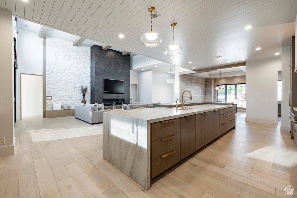 Kitchen with modern cabinets, open floor plan, a large island, light wood-type flooring, and light stone counters