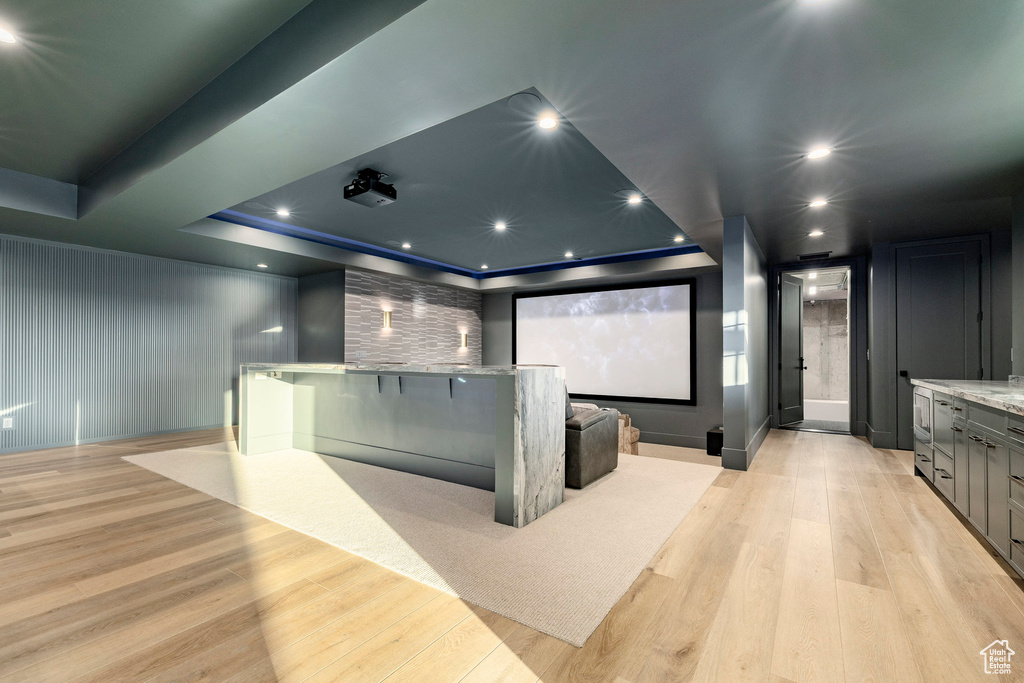 Home theater with light wood-type flooring, a raised ceiling, and recessed lighting