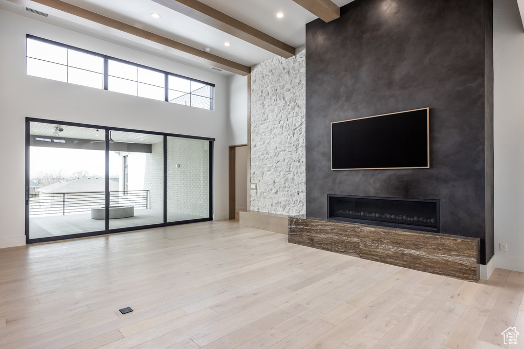 Unfurnished living room featuring a fireplace, wood finished floors, visible vents, beamed ceiling, and a towering ceiling