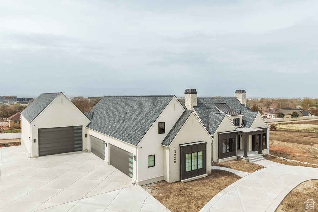 Modern farmhouse featuring driveway, a shingled roof, a chimney, and stucco siding