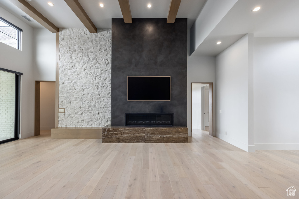 Unfurnished living room with beamed ceiling, a high ceiling, wood finished floors, and a large fireplace