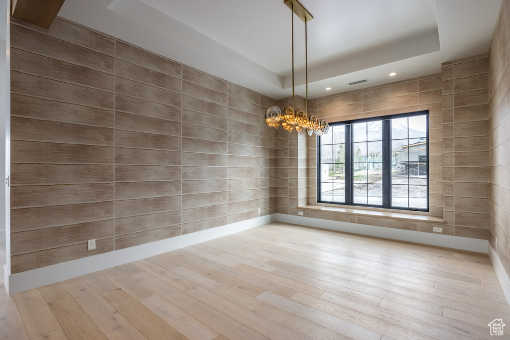 Unfurnished room with a notable chandelier, visible vents, wood finished floors, and a raised ceiling