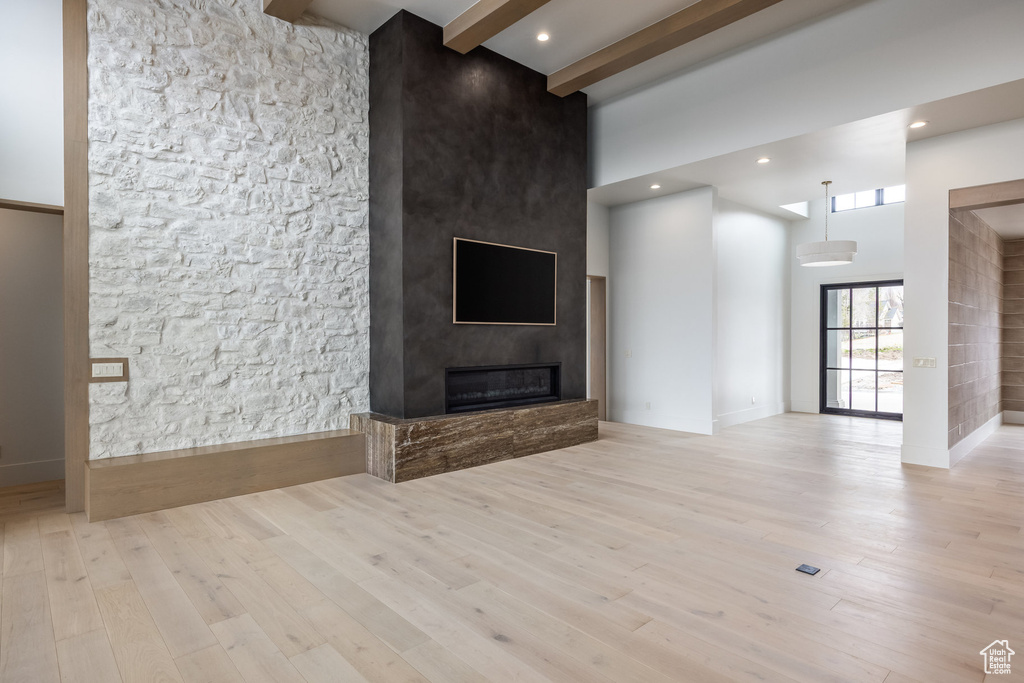 Unfurnished living room featuring a towering ceiling, wood finished floors, beam ceiling, and a large fireplace