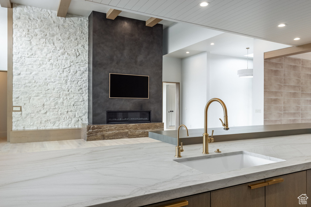 Kitchen featuring a sink, a fireplace, light stone countertops, beamed ceiling, and recessed lighting
