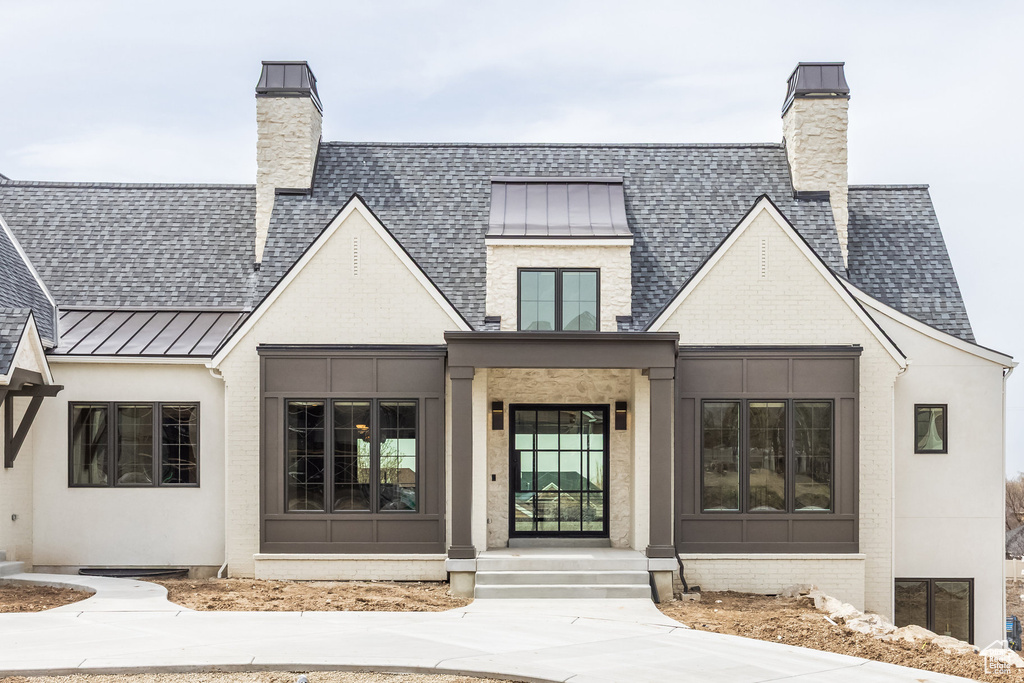 Exterior space featuring a chimney, a shingled roof, a standing seam roof, and brick siding
