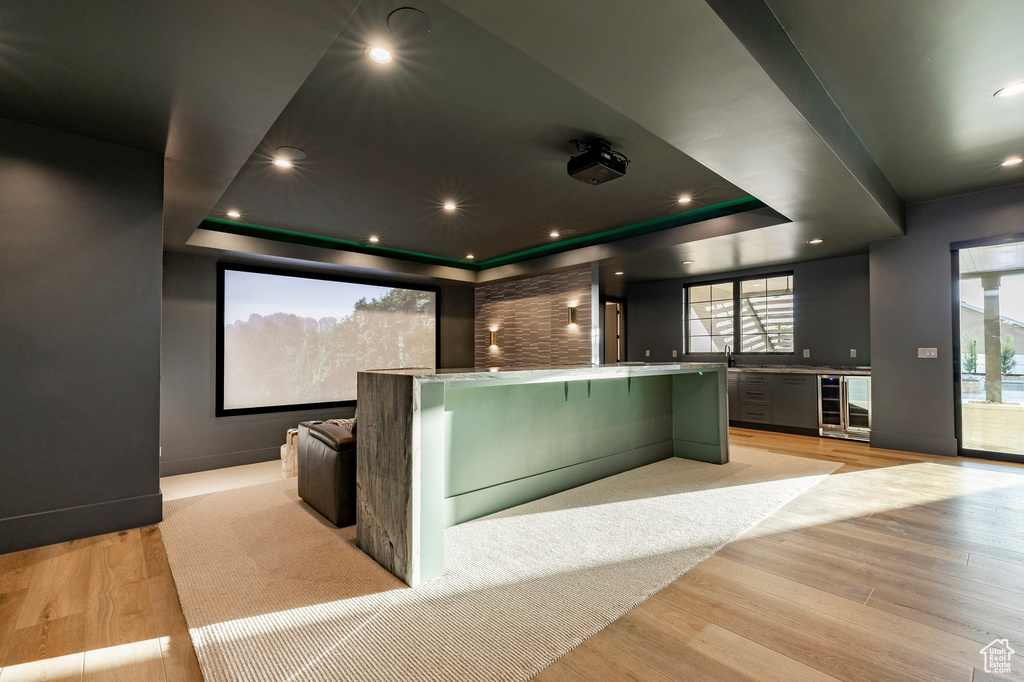 Home theater featuring wine cooler, a tray ceiling, light wood finished floors, and a community bar