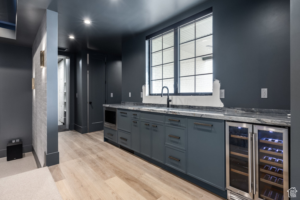 Kitchen with stainless steel microwave, a sink, stone counters, light wood-style floors, and beverage cooler