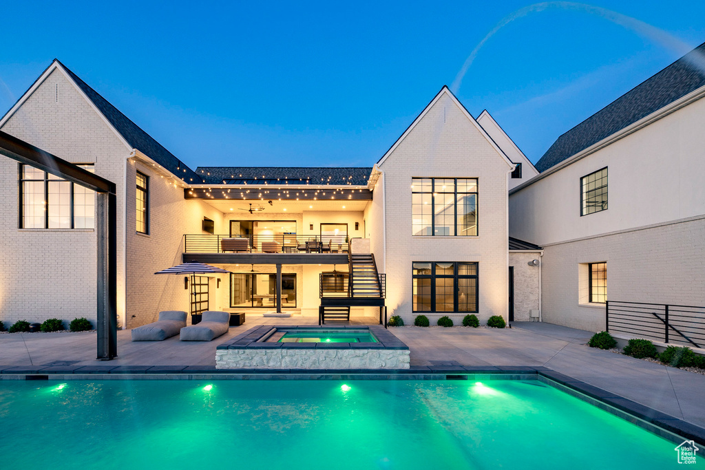 Rear view of property with an in-ground hot tub, a balcony, a patio, an outdoor pool, and stairs